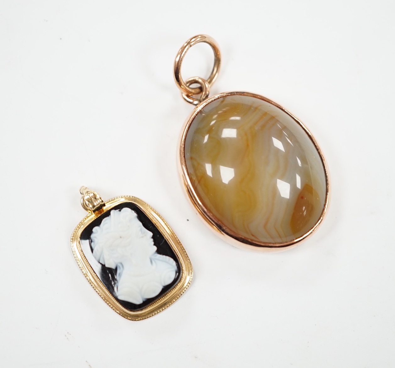 A yellow metal mounted oval banded agate pendant, 26mm and a smaller yellow metal mounted sardonyx cameo pendant.